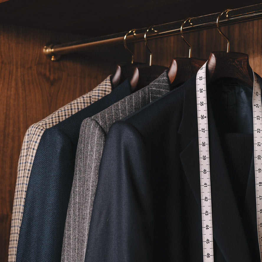 Dark suits hanging on a rack with a measuring tape, in a wooden wardrobe.