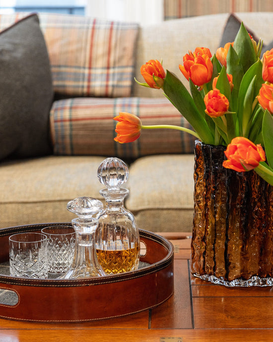 Crystal whisky decanter and glasses on a leather tray at the Huntsman Club at 11 Savile Row - with Huntsman tweed sofa and orange tulips