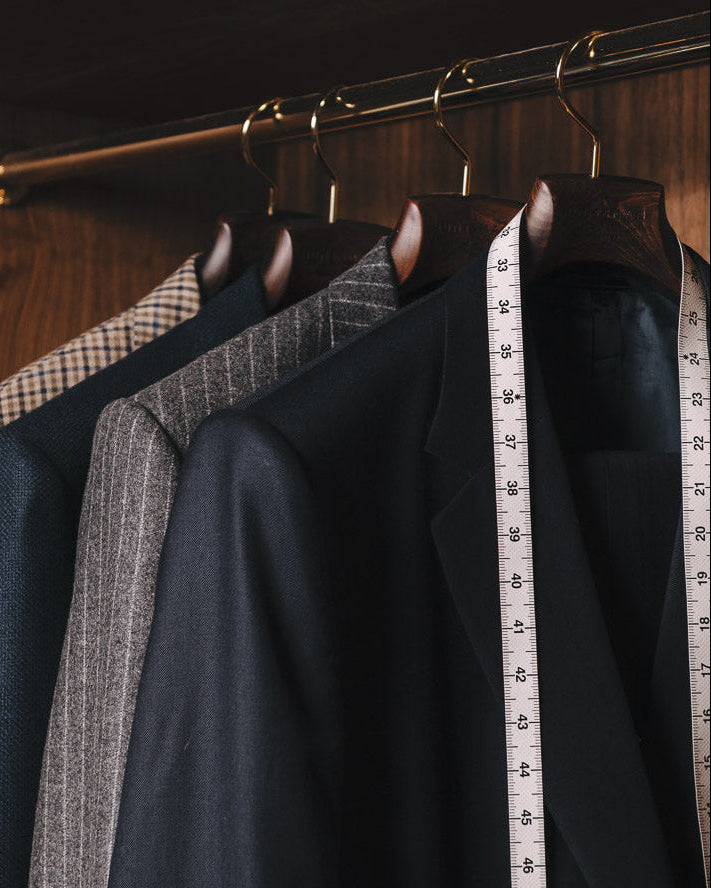 Dark suits hanging on a rack with a measuring tape, in a wooden wardrobe.
