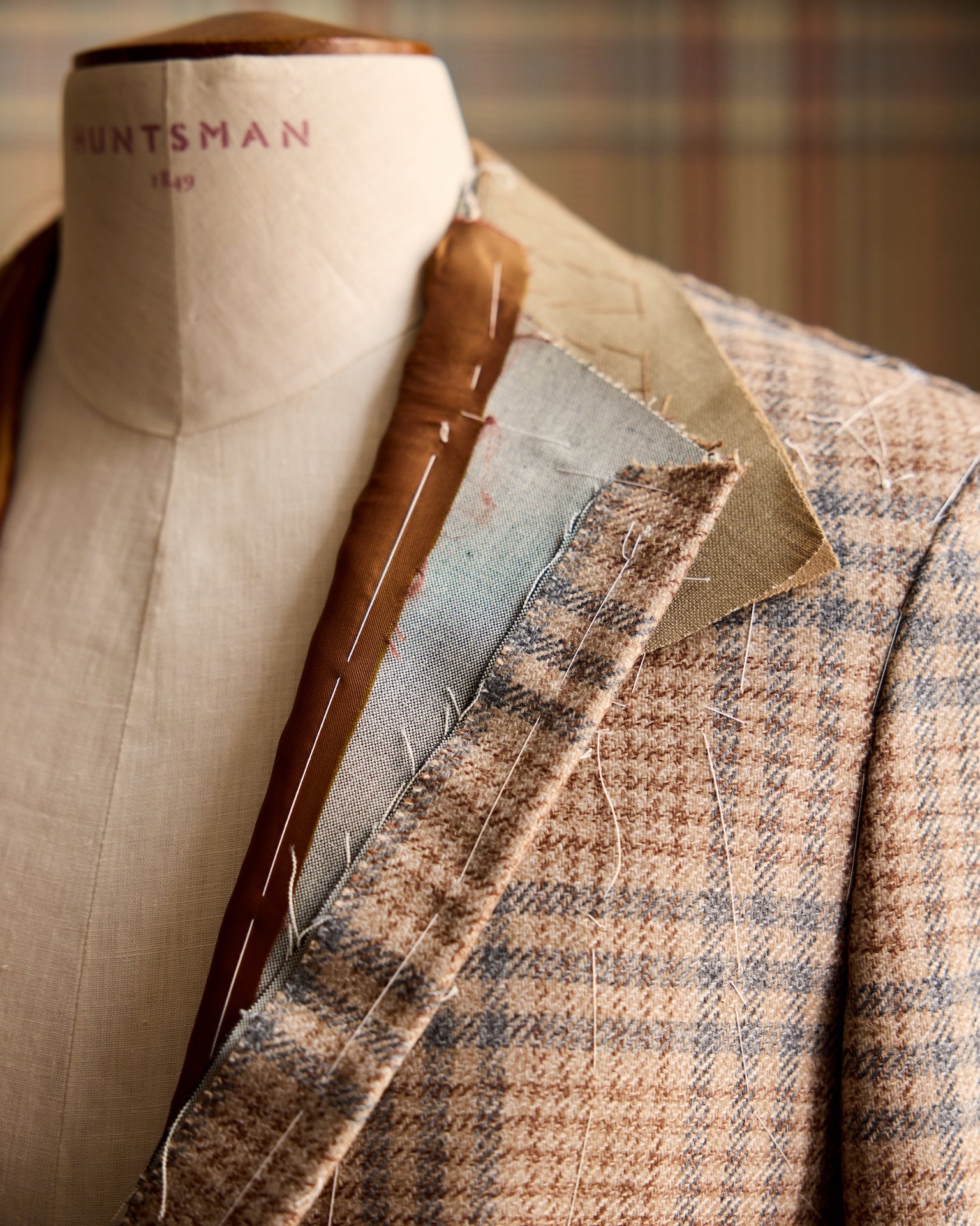 Close-up of a suit jacket with plaid pattern on a mannequin, featuring the brand 'Huntsman'.