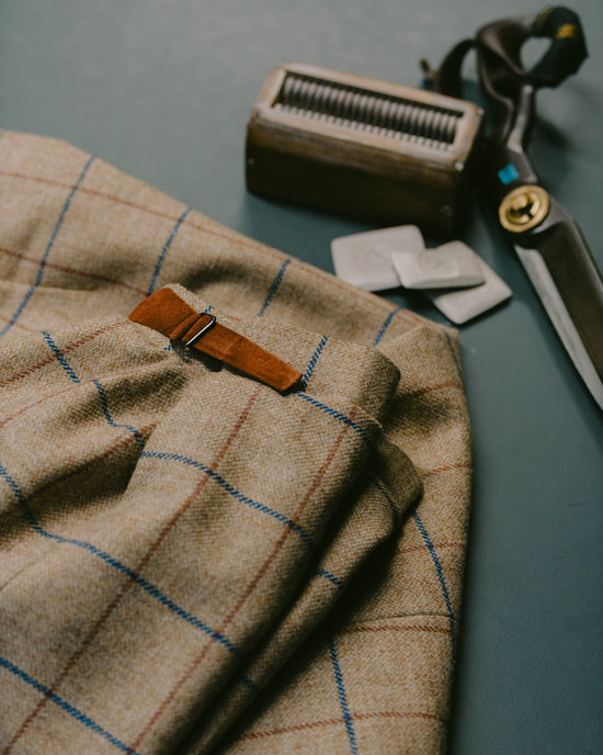 Huntsman bespoke tweed shooting breeks lay on cutting table with a cutters tools - chalk and shears at 11 Savile Row