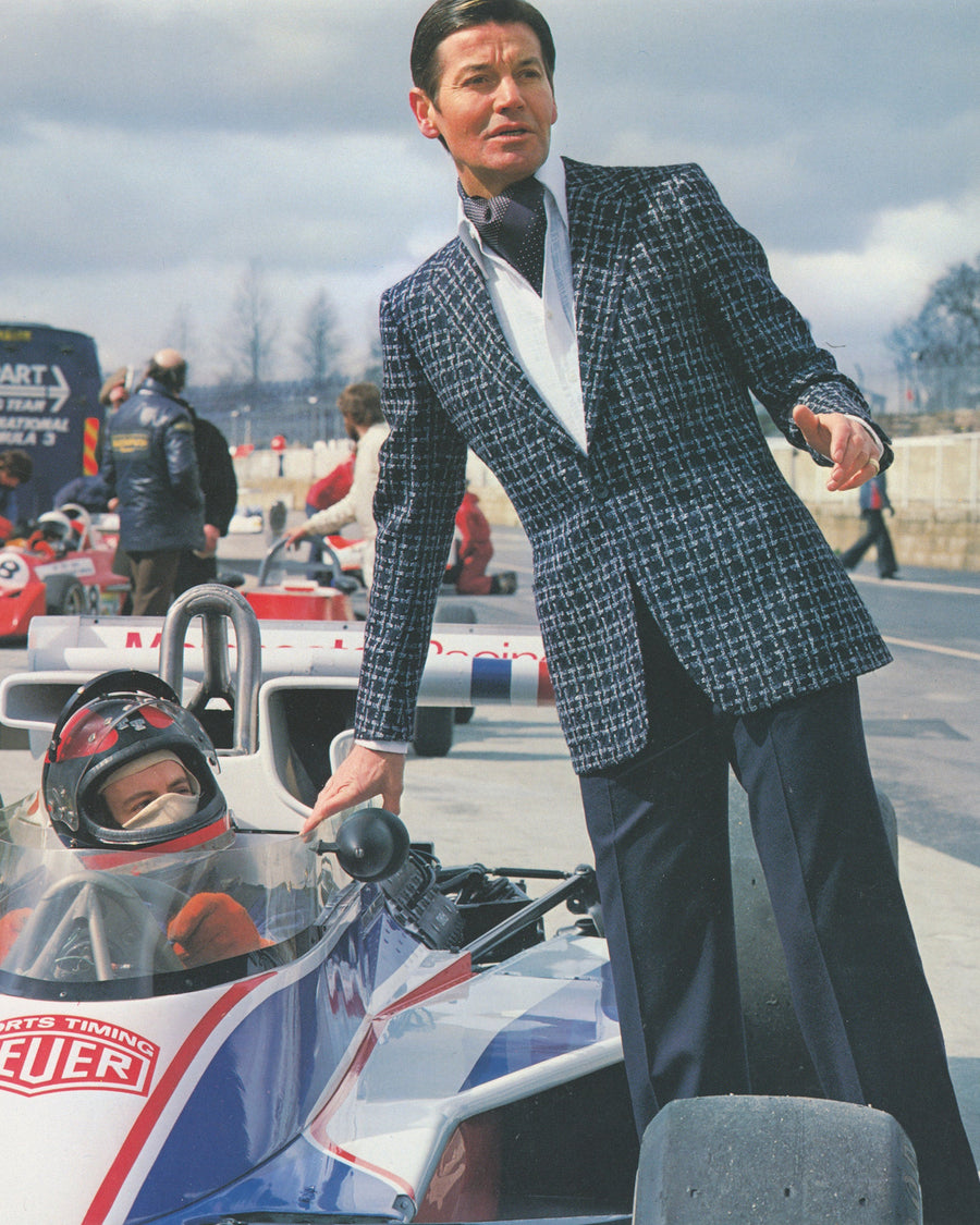 Huntsman archive campaign, model in signature one-button silhouette stands by racing car driver, track side
