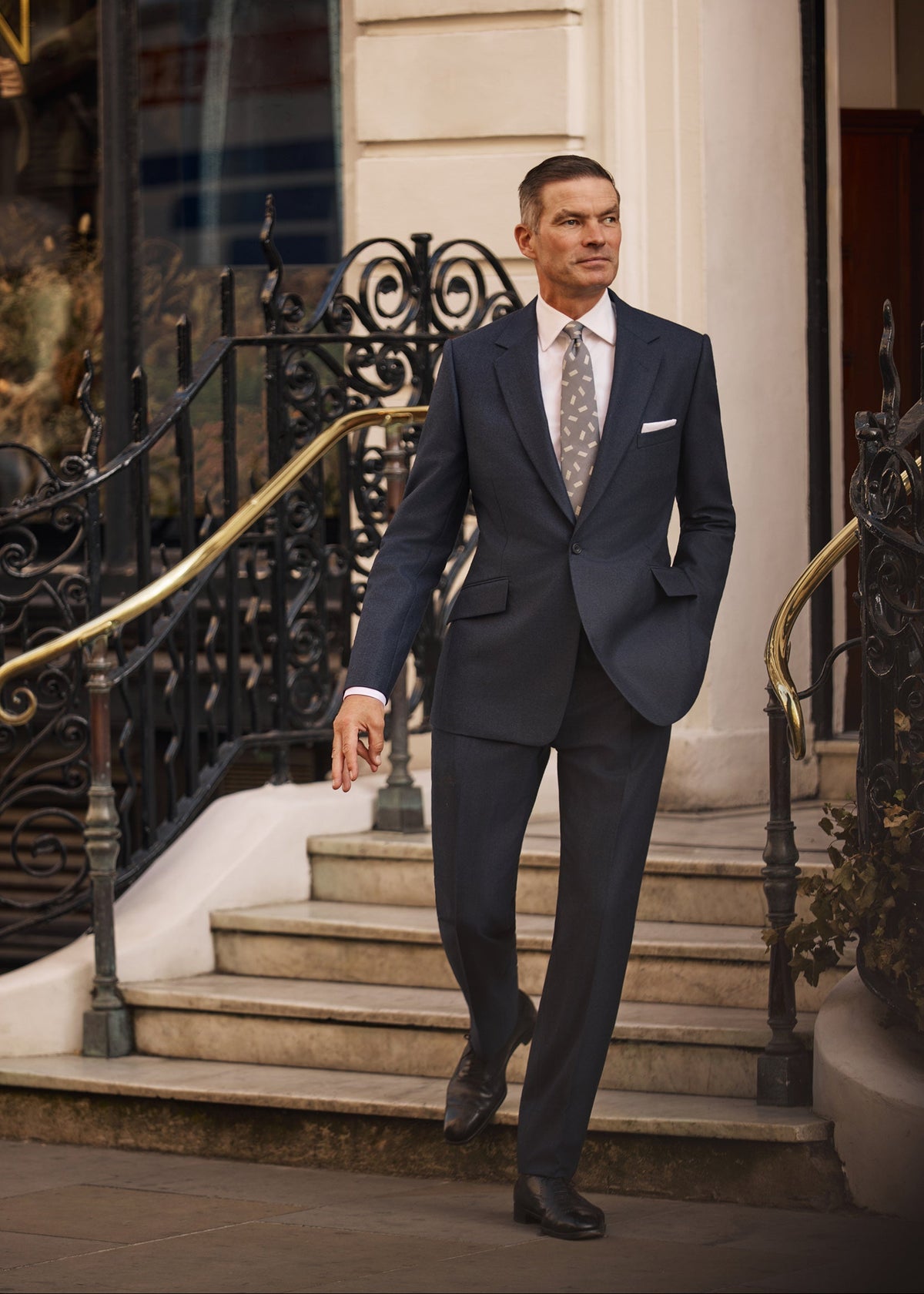 Huntsman navy heritage twill suit, walking down the steps outside the Huntsman Savile Row shopfront, AW26 campaign.